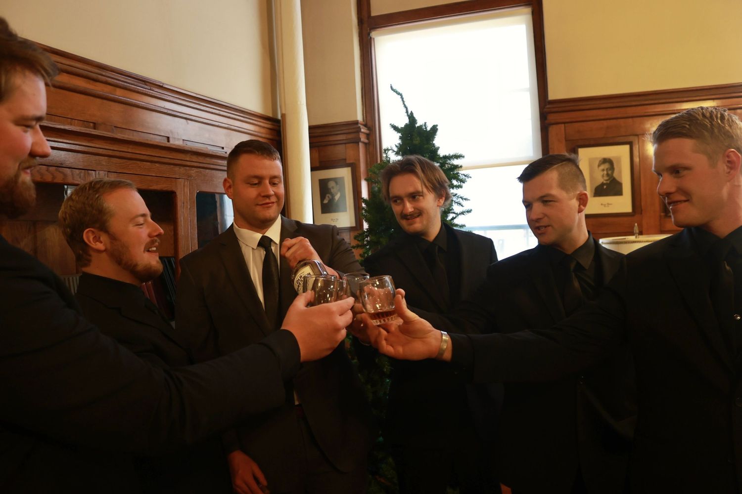 People in dark suits standing together in an indoor setting with wooden decor.
