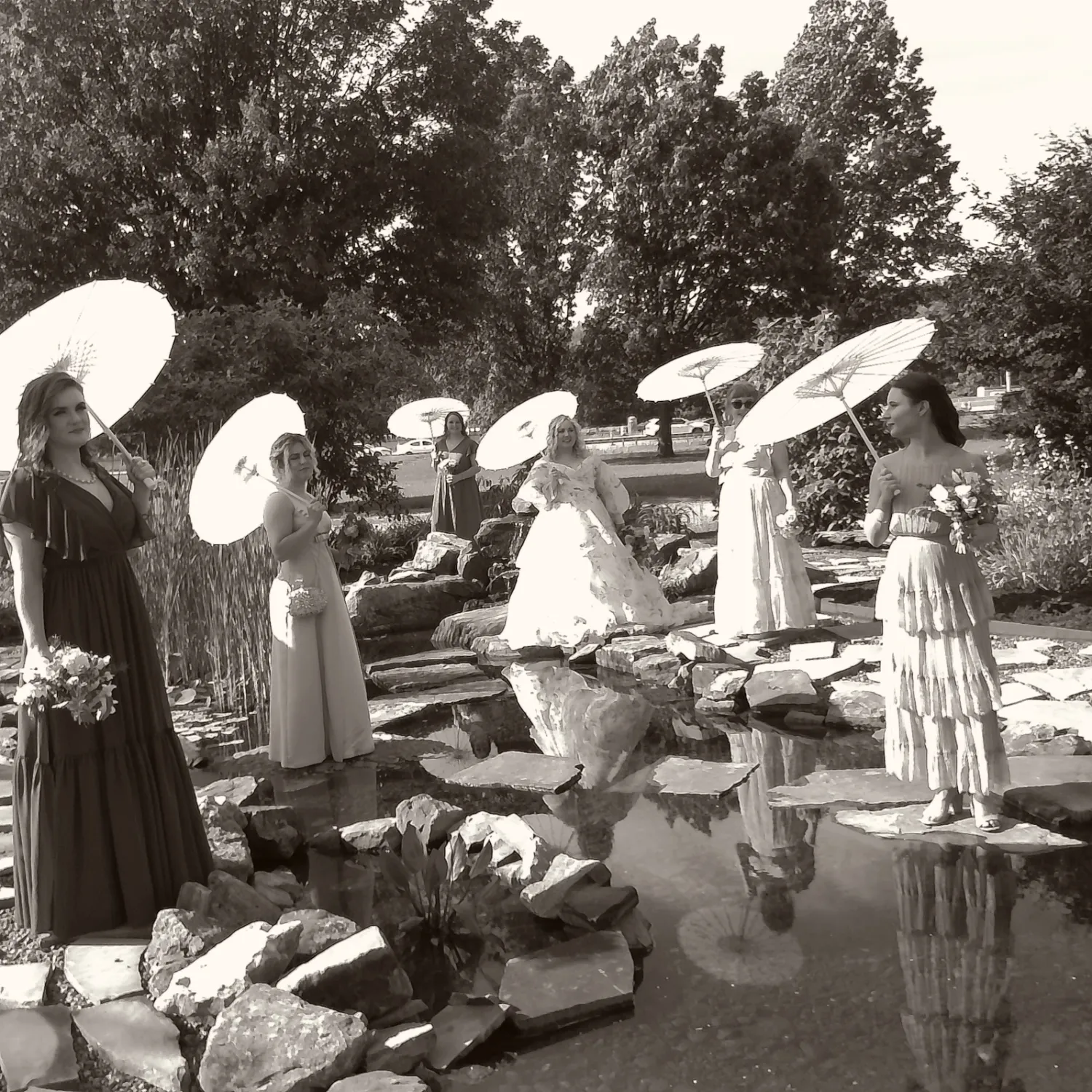 A group of people in white clothing and sun hats gather outdoors for a social event in a black and white photograph.