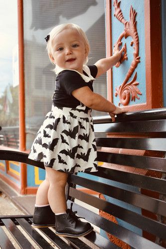 Child wearing bat print outfit climbing on wooden bench.