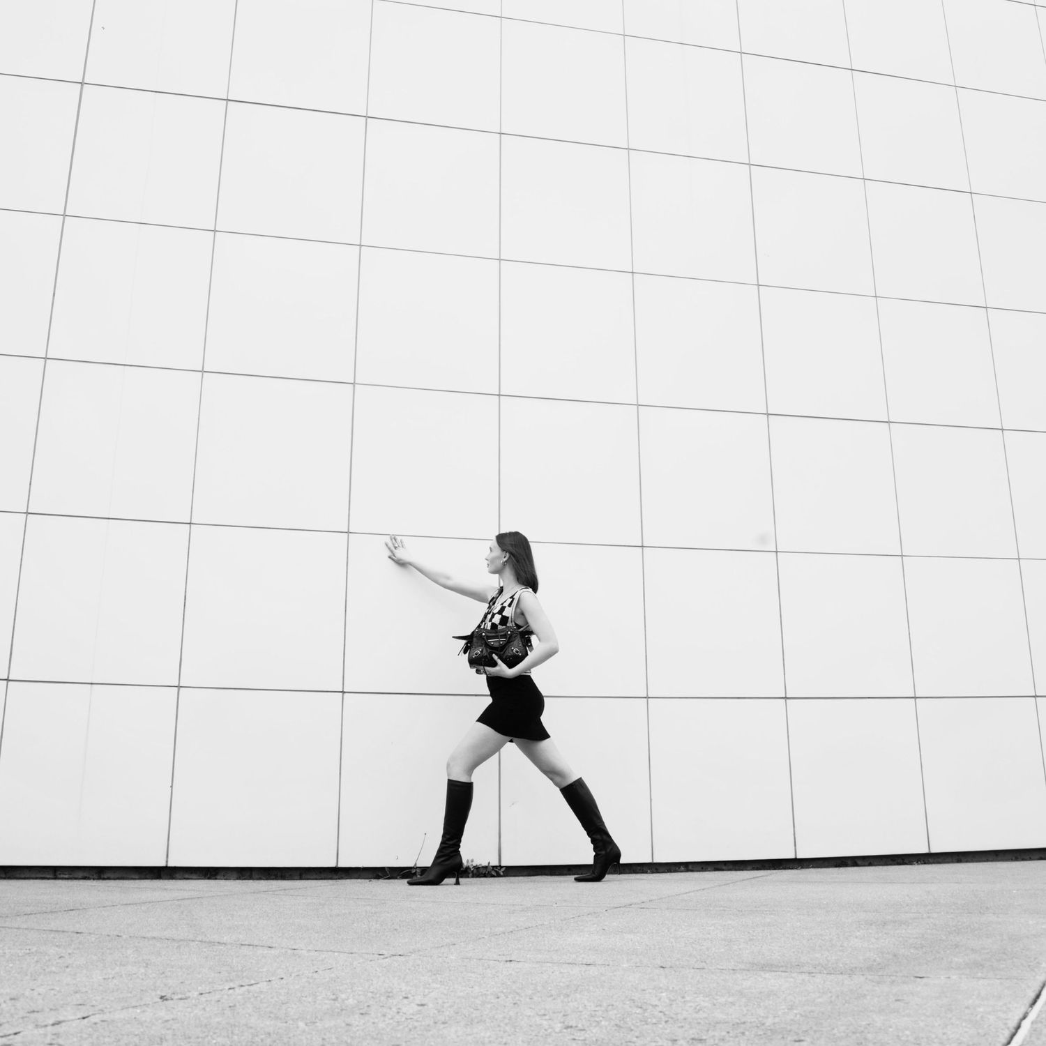 Minimalist black and white composition showing a person walking against a stark white wall with dramatic shadows.