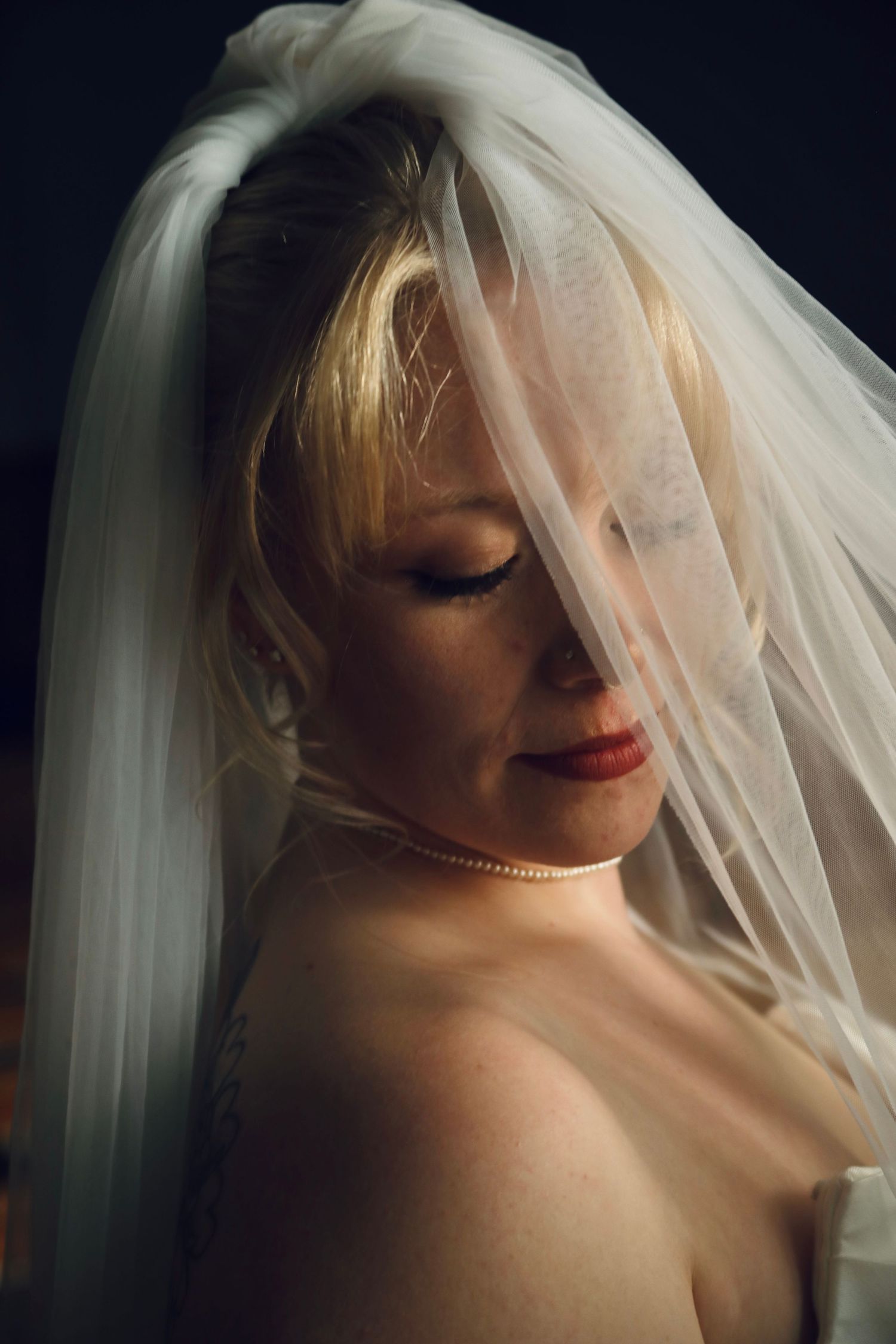 Artistic bridal portrait with delicate veil in moody lighting.