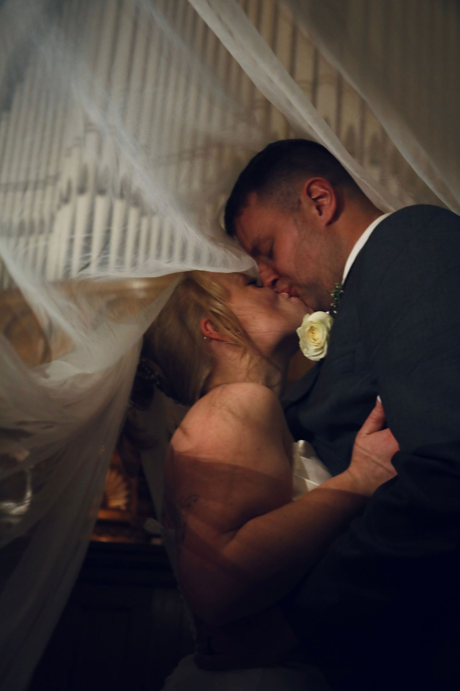 Romantic wedding moment under flowing white veil with boutonniere detail.