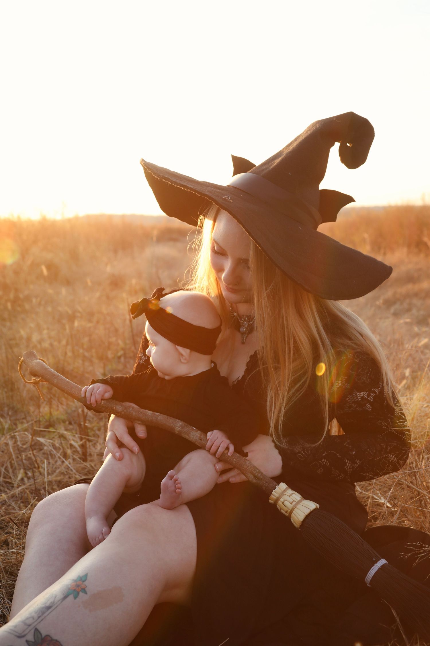 Person in witch costume sitting in golden field at sunset.