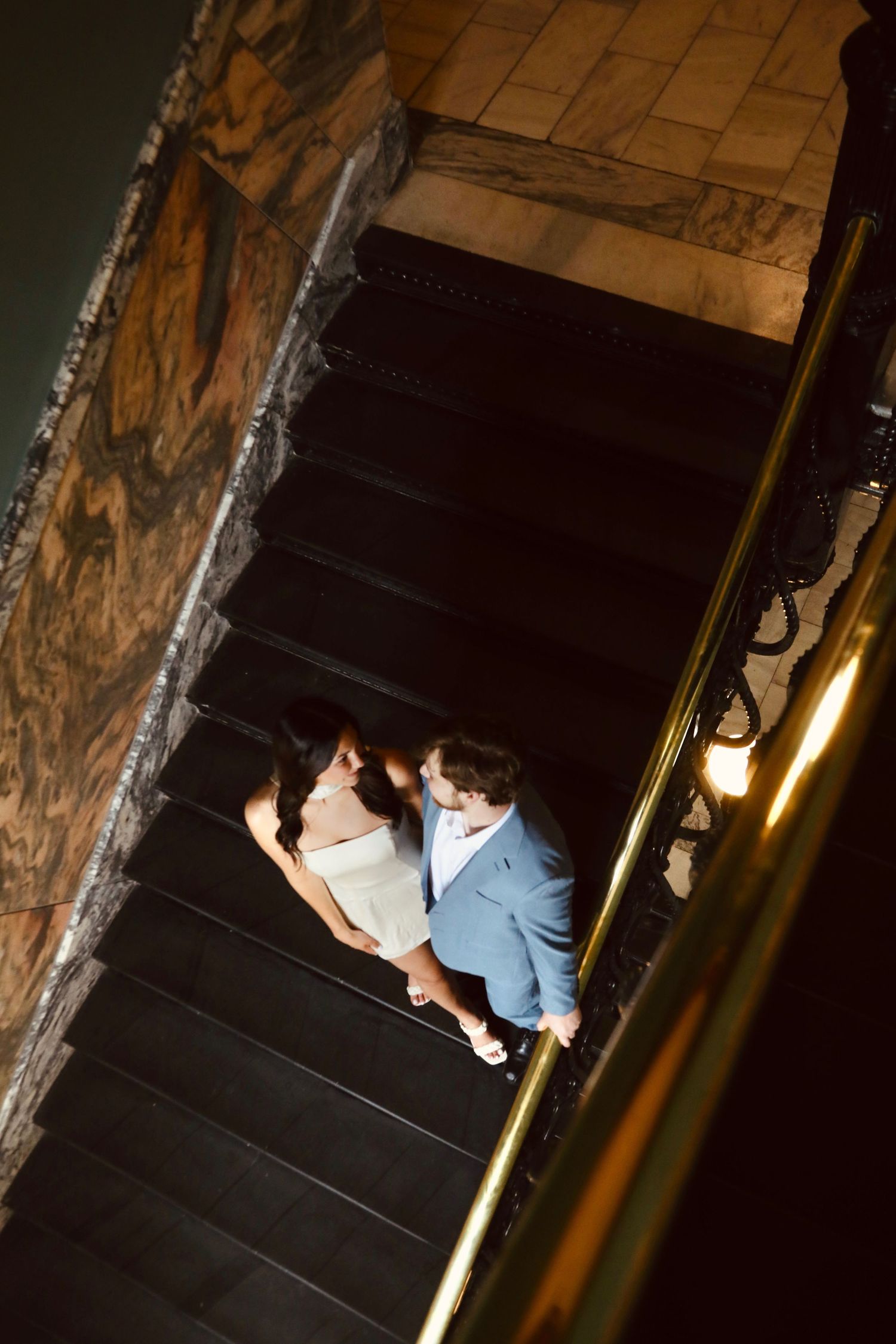 Couple ascending dimly lit stone stairs with dramatic shadows.