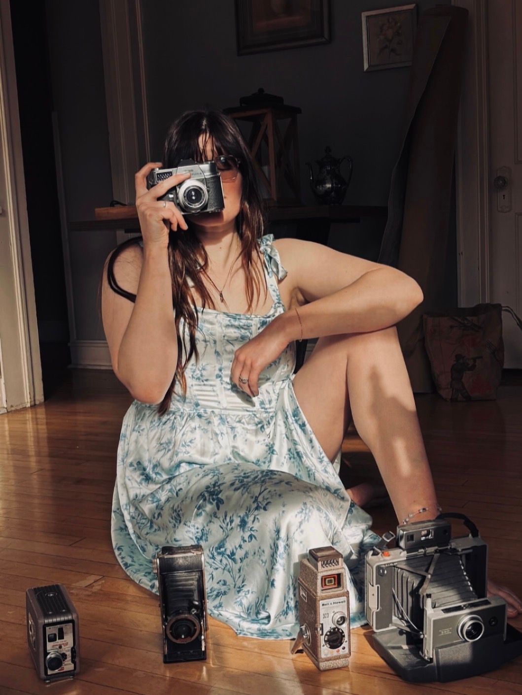 Collection of vintage cameras arranged on wooden floor with person in floral dress.