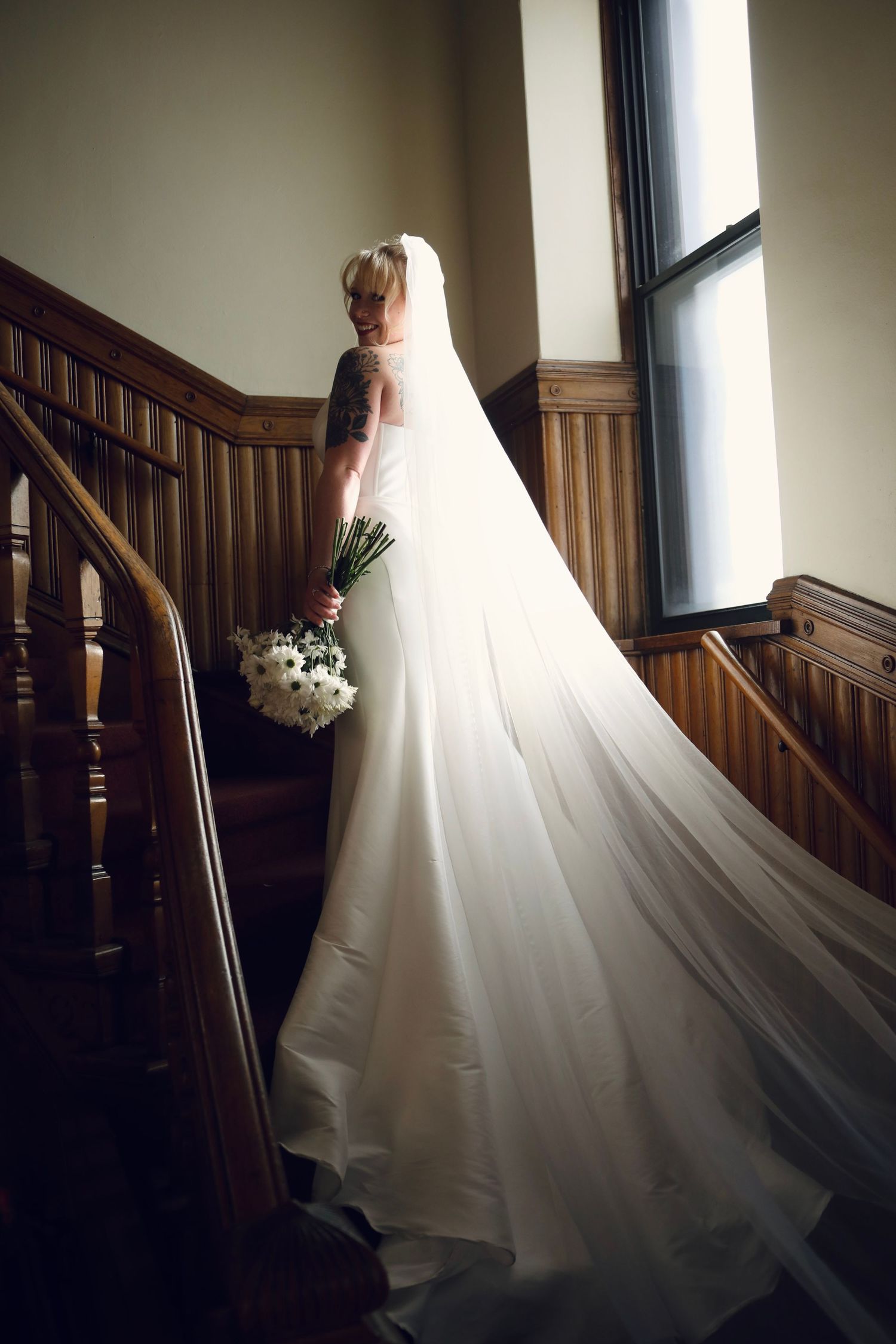 Dramatic bridal portrait on wooden staircase with long flowing veil and white bouquet.