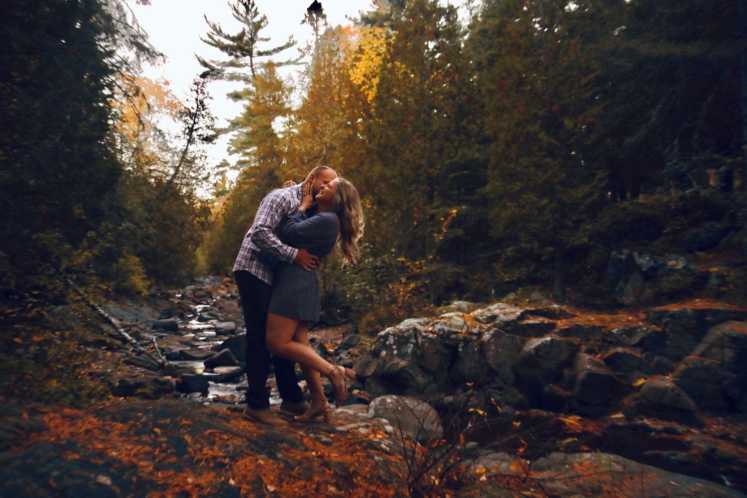 A person explores a rocky creek bed surrounded by autumn foliage and evergreen trees in a forest setting.