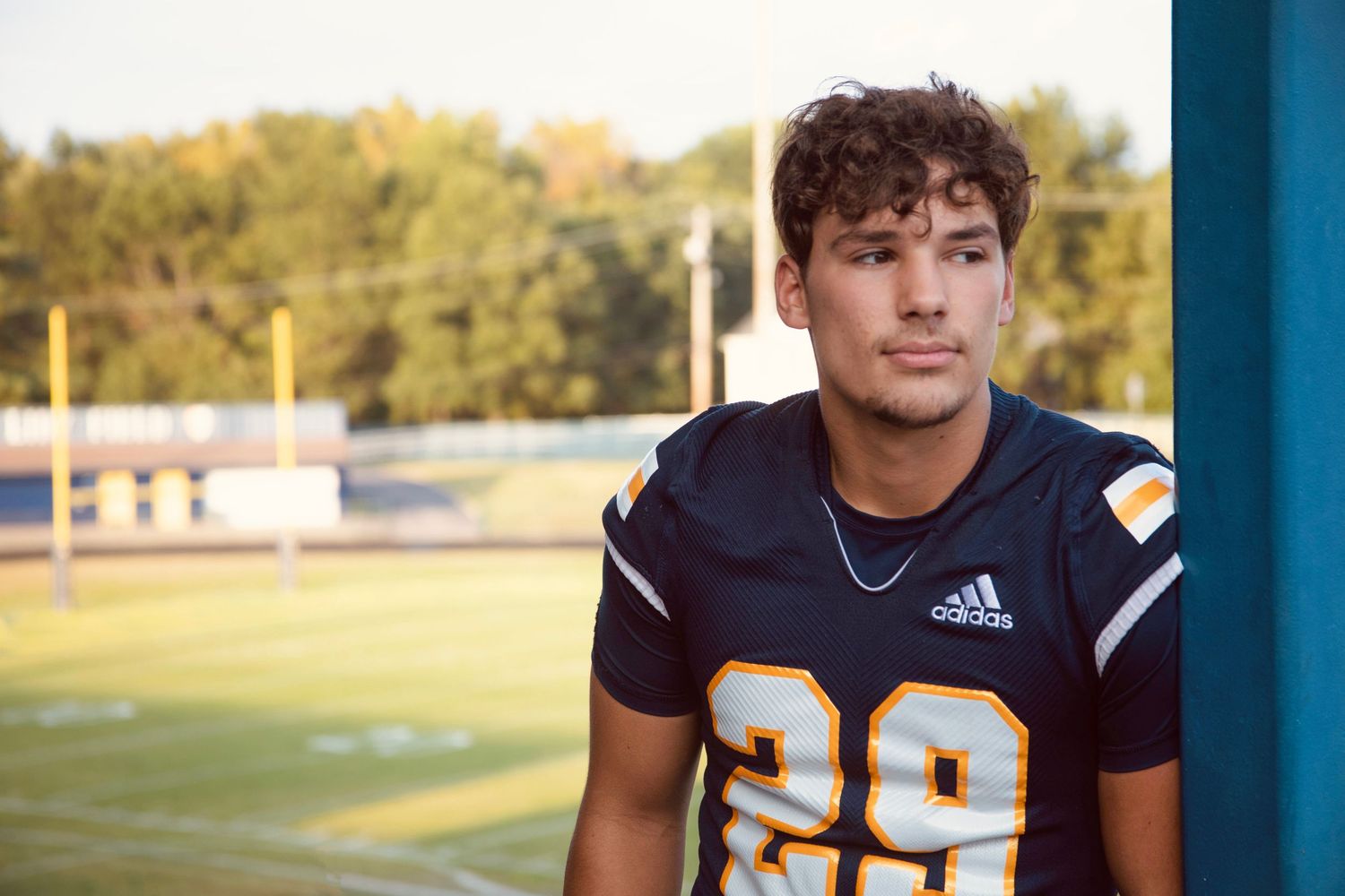 A collage of high school football players in navy blue jerseys posing for individual portrait photos outdoors.