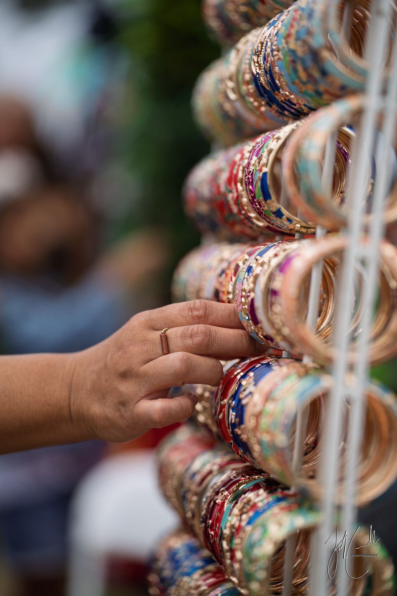 Colorful bangles and bracelets displayed on rack with hand reaching to touch them.