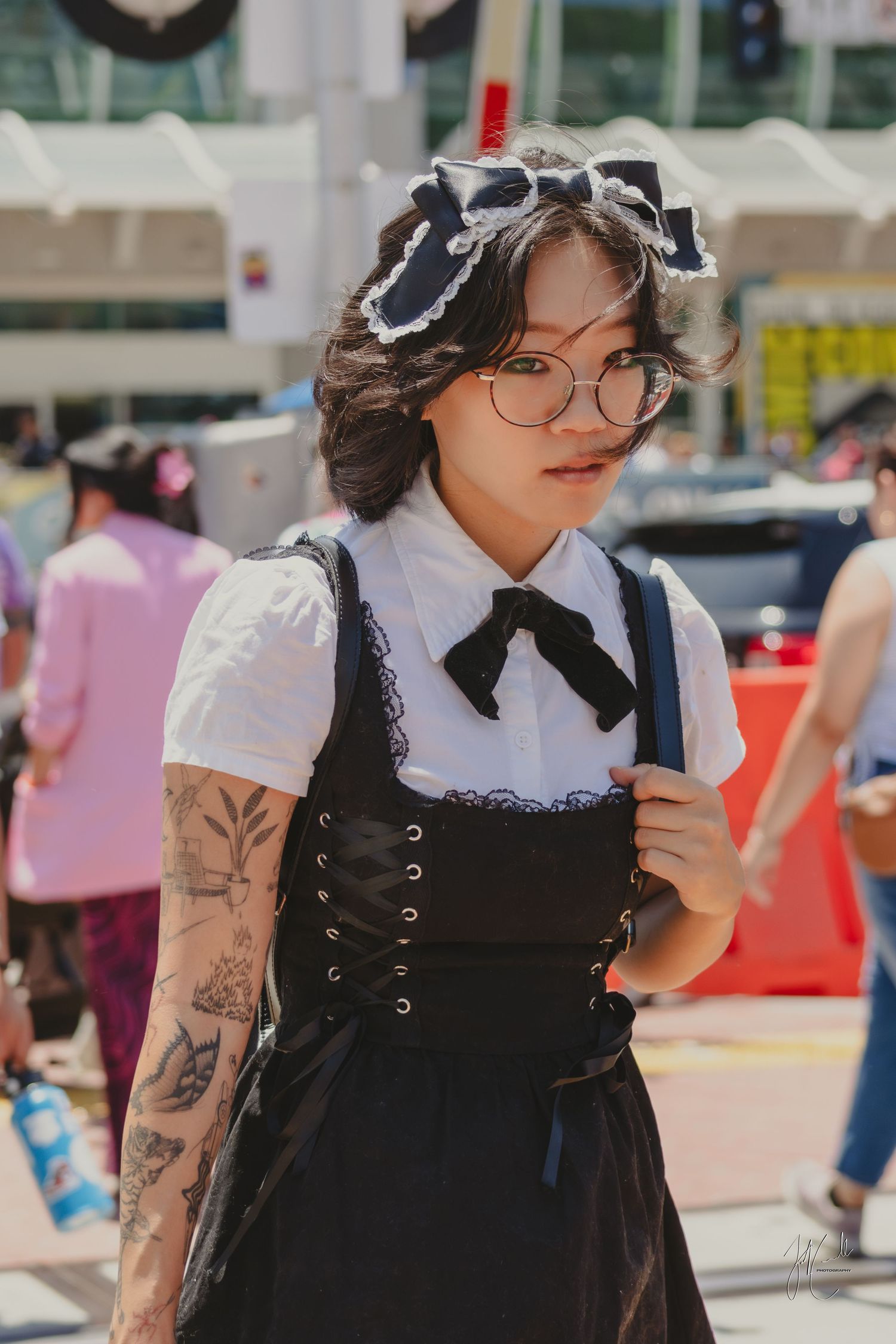 Person in gothic lolita style dress with black apron, white collar, and visible tattoos on their arm.