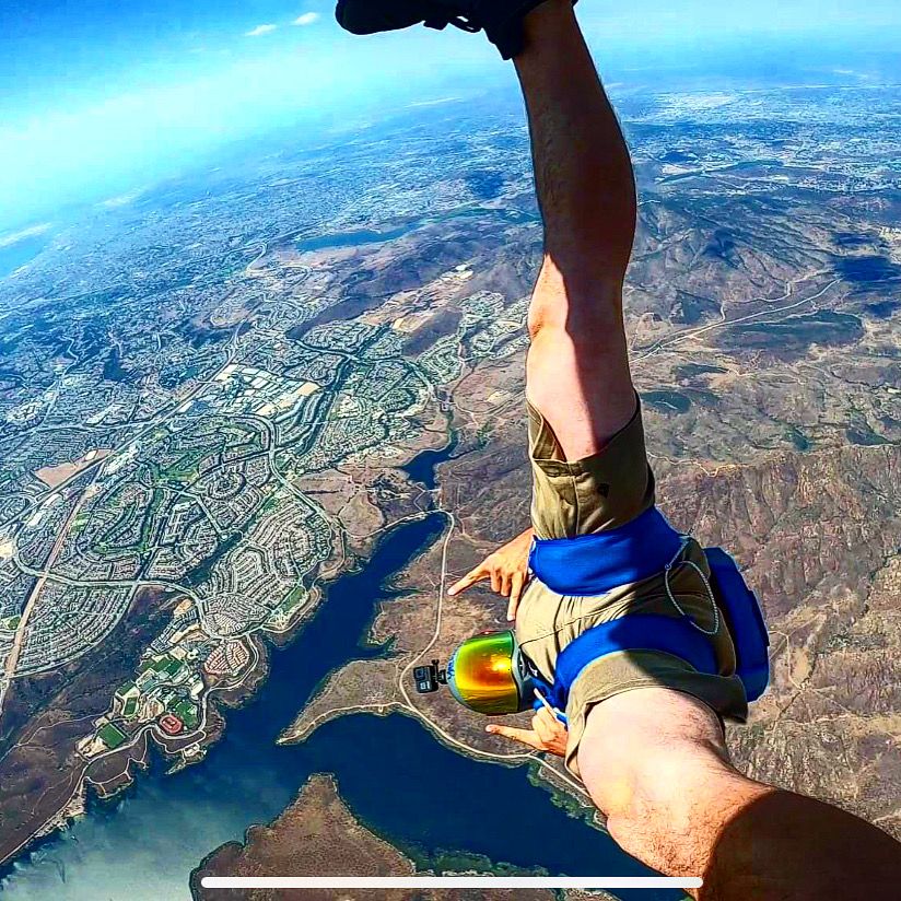 Aerial view of a skydiver soaring above mountains and lakes with blue skies in the background.
