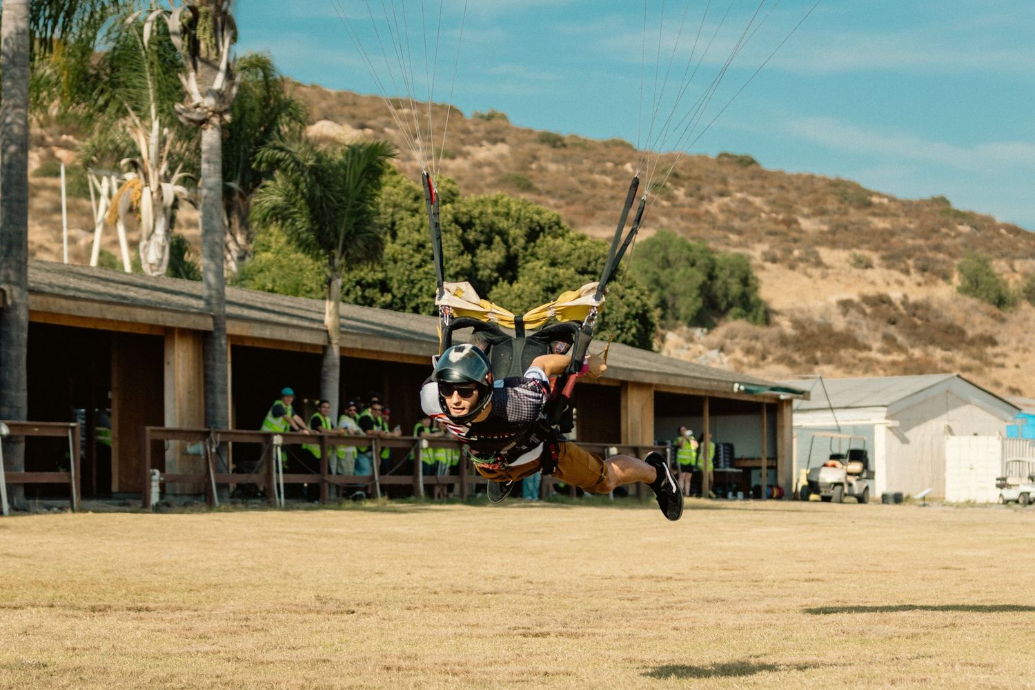 Skydiver performing aerial maneuvers against a backdrop of mountains and desert terrain.