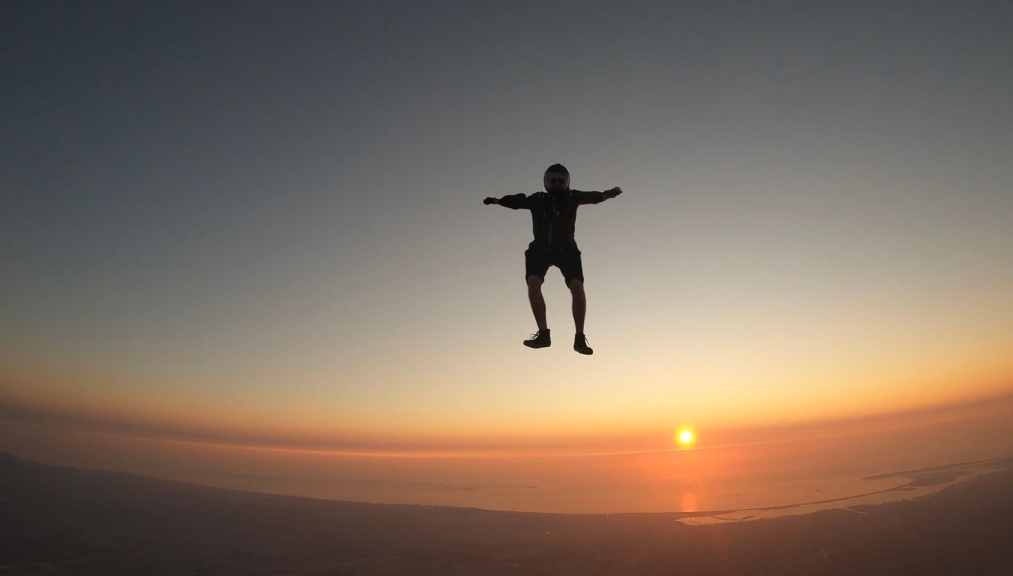 Silhouette of a person skydiving against a dramatic sunset sky.