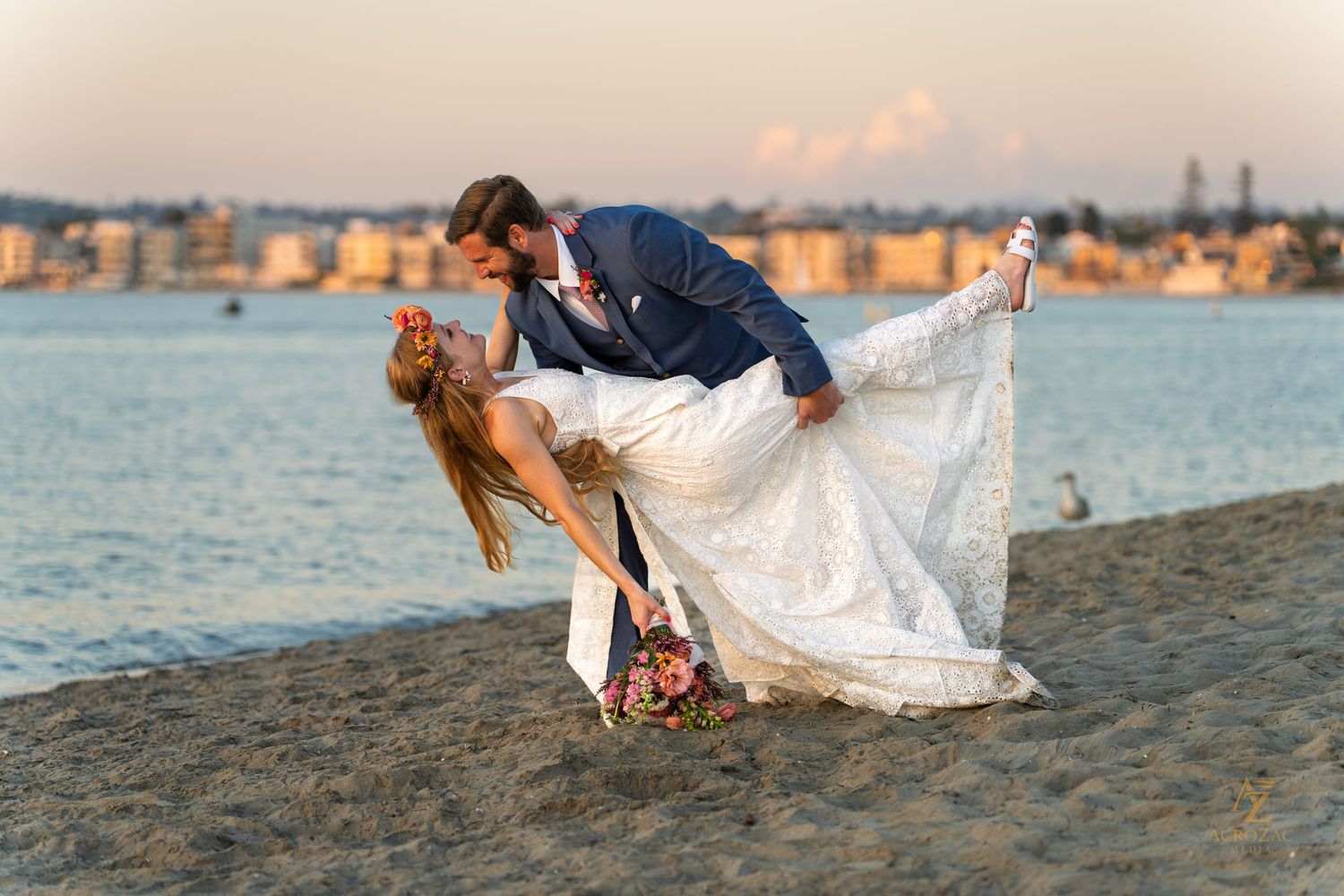 Playful wedding photo shoot on beach with couple in dramatic dip pose.