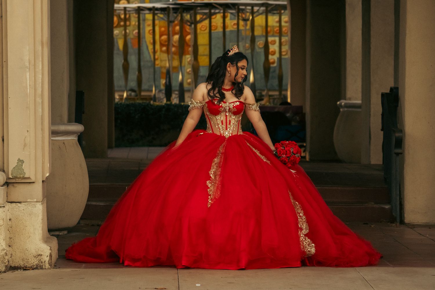 A row of elegant red quinceañera dresses displayed in an ornate hallway with marble columns.
