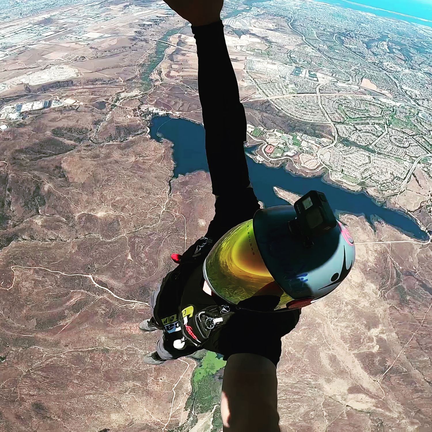 Skydiver's perspective looking down at mountainous terrain and waterways during freefall.