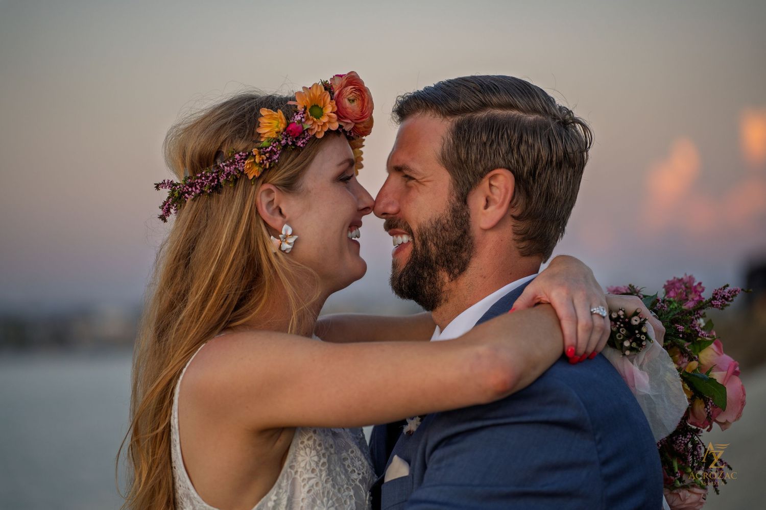 Romantic couple embracing at sunset with floral crown and waterfront view.