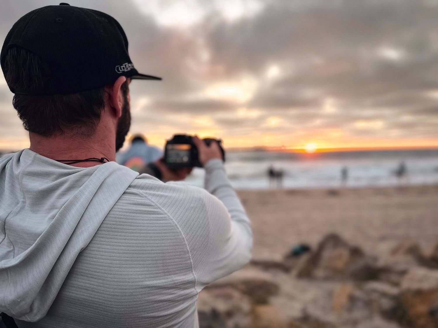 Photographer capturing sunset at beach with mobile phone during golden hour.