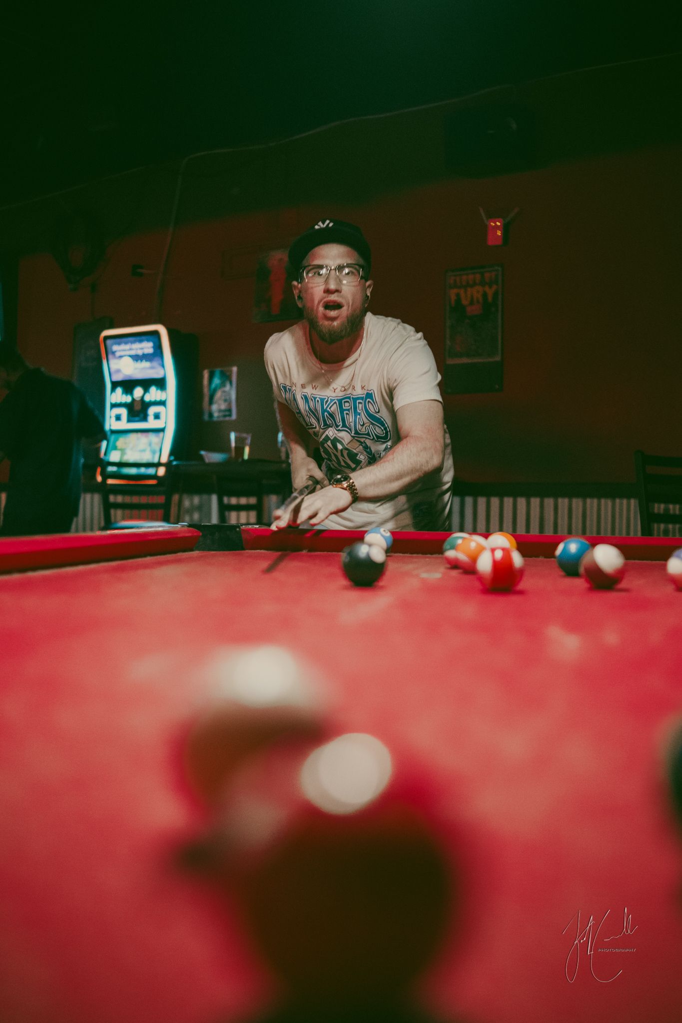People gathered around a red pool table in a dimly lit game room.