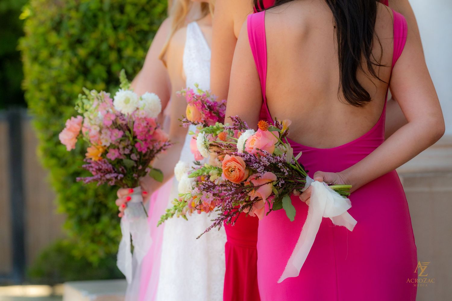 Bridesmaids in bright pink dresses holding colorful floral bouquets.
