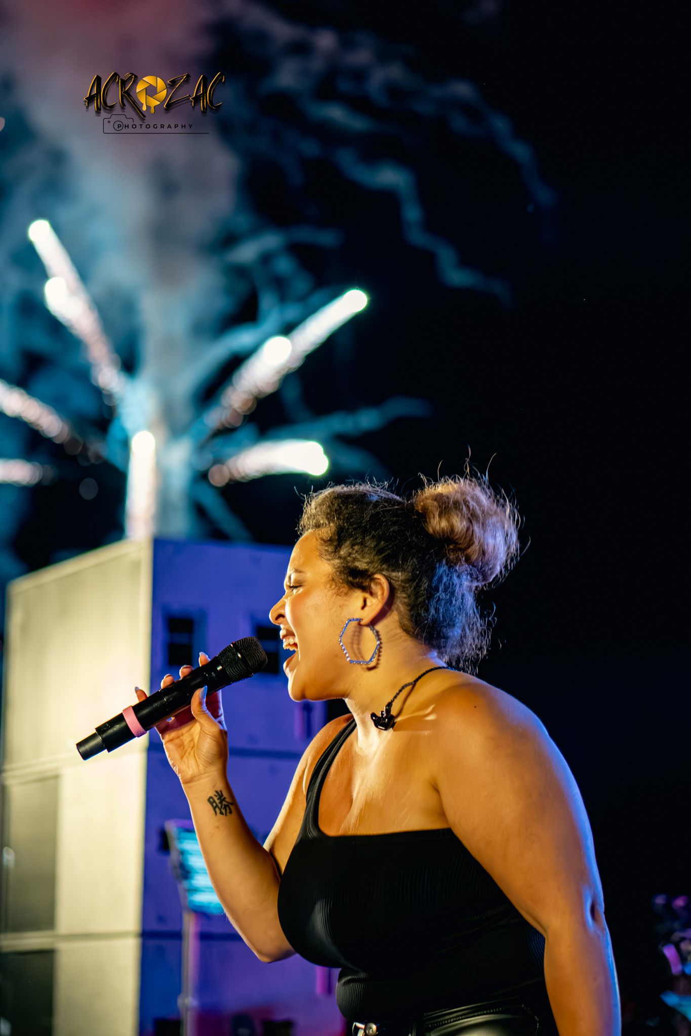 Concert performer singing passionately on stage with dramatic blue lighting and smoke effects in the background.