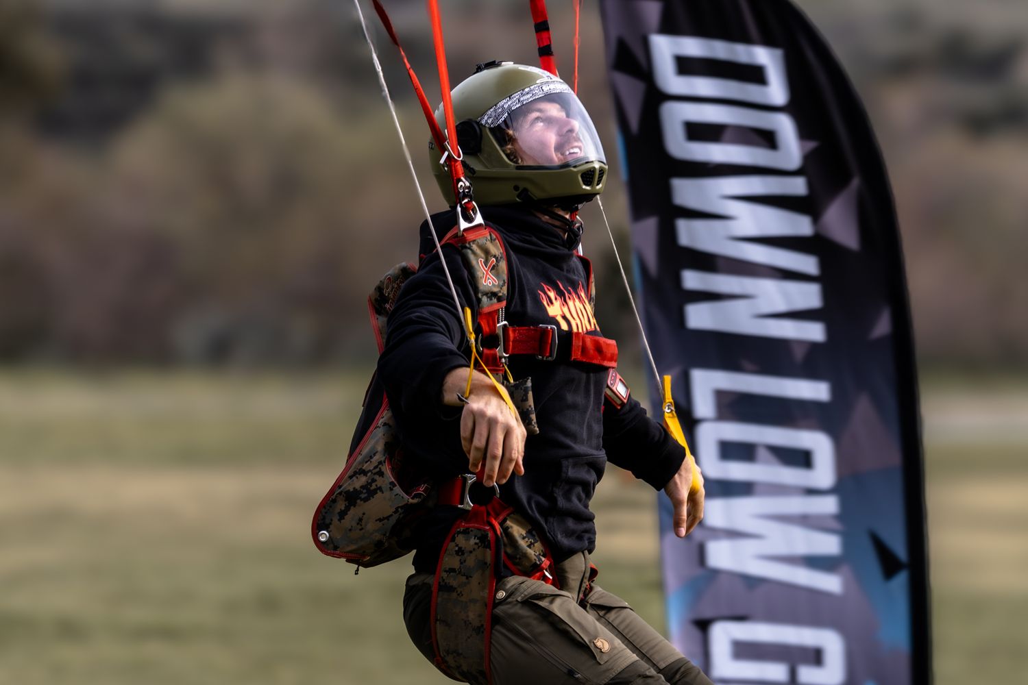 Skydiver in black and red gear performs maneuvers near a landing zone flag.