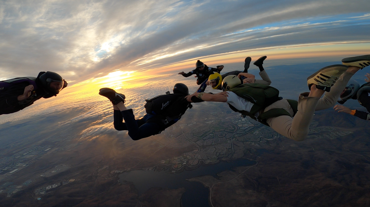 Panoramic view of skydivers in formation against clouds during golden hour.