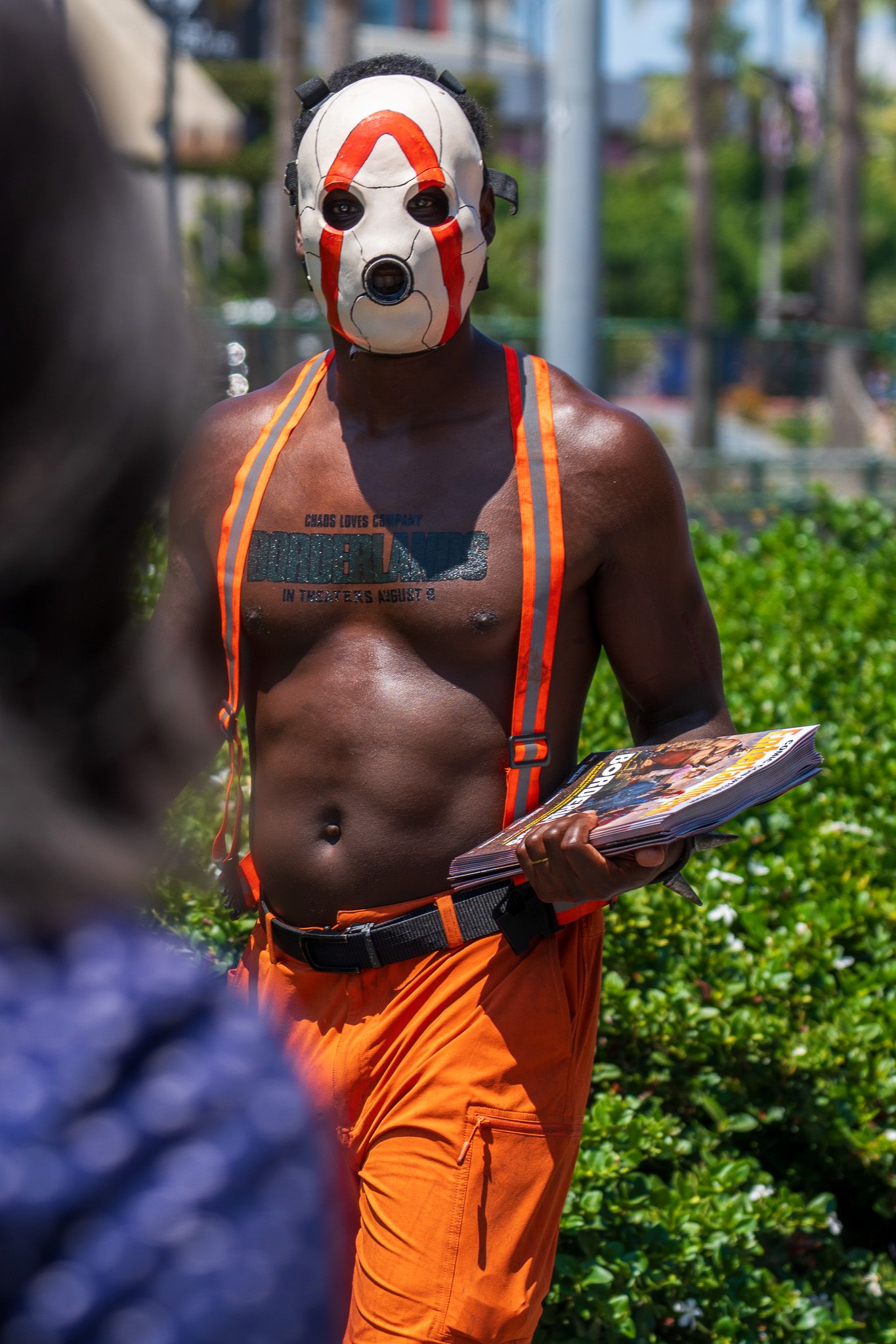 Person in orange overalls and white mask posing with props against urban background.