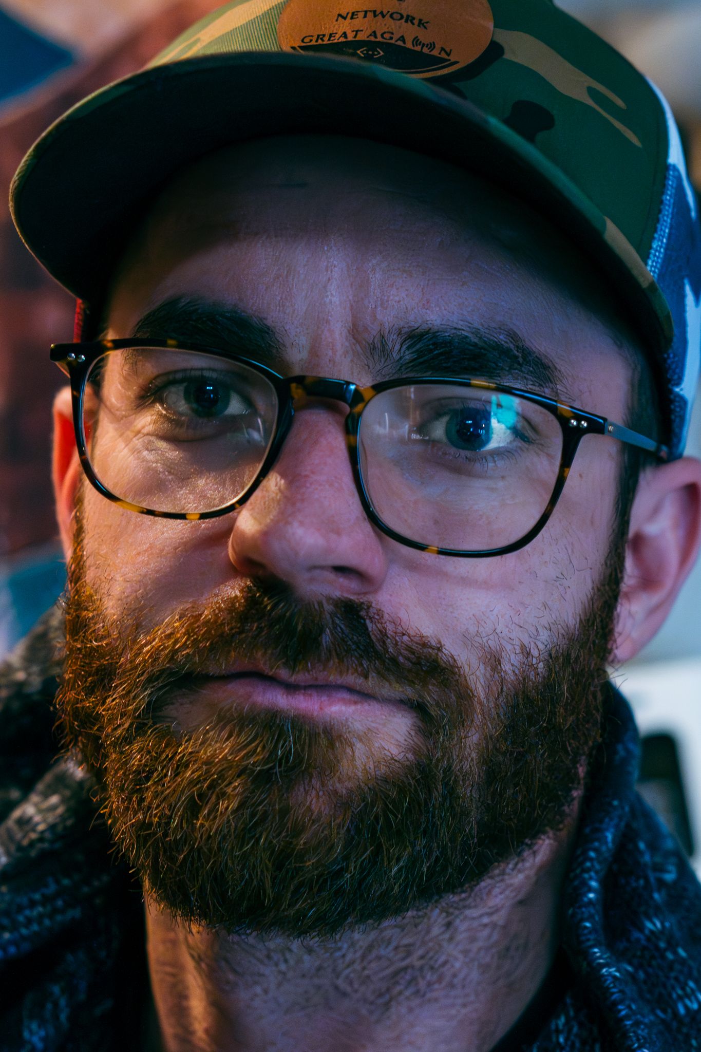 Close-up portrait of someone wearing glasses and a baseball cap with a full beard.