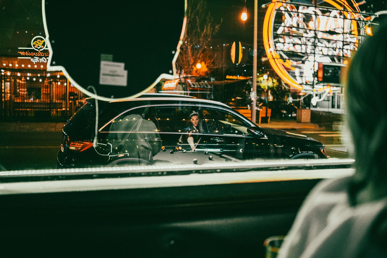 Night street scene viewed through car window with neon lights reflecting.