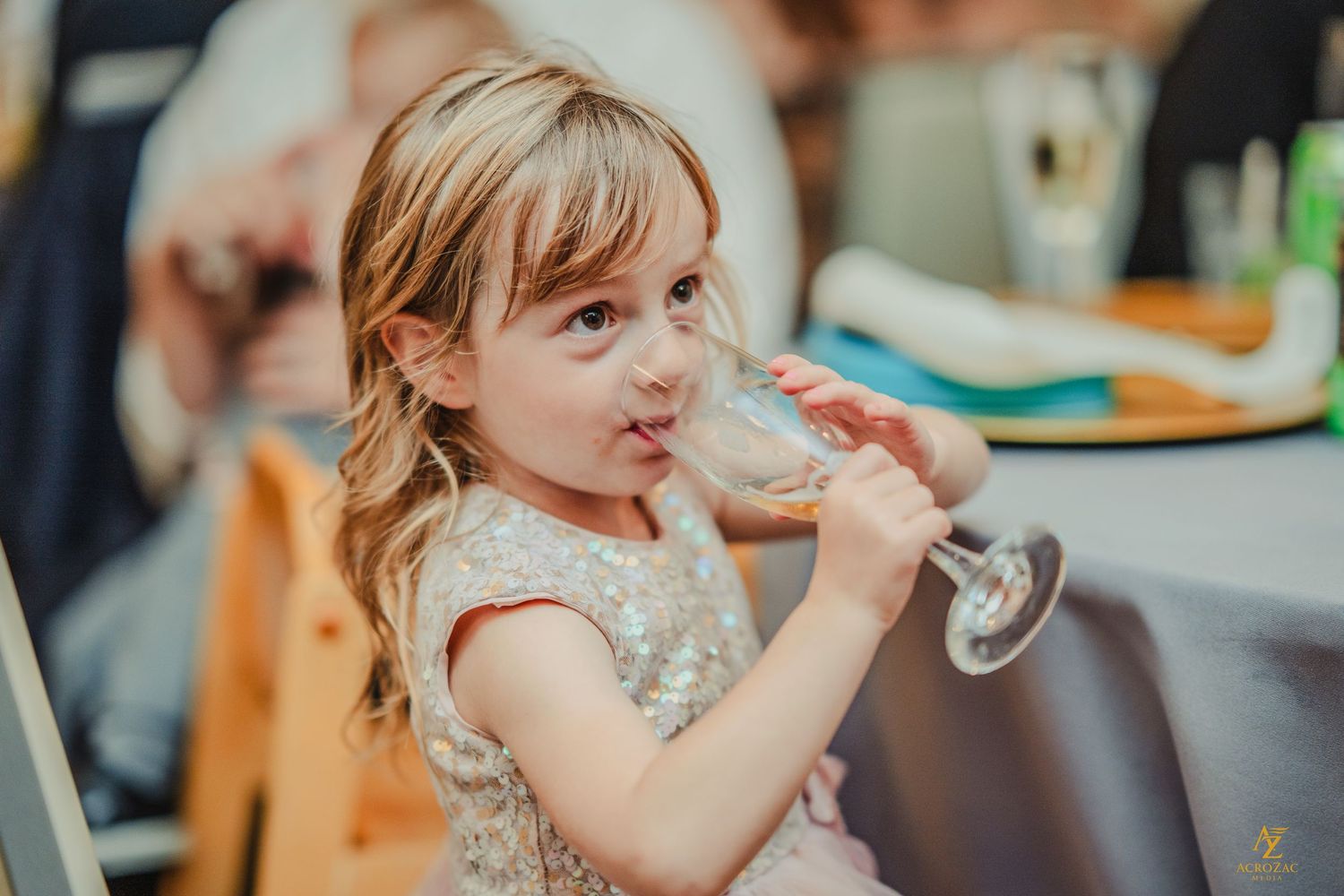 Young person in sparkly dress sipping from a champagne glass at a celebration.