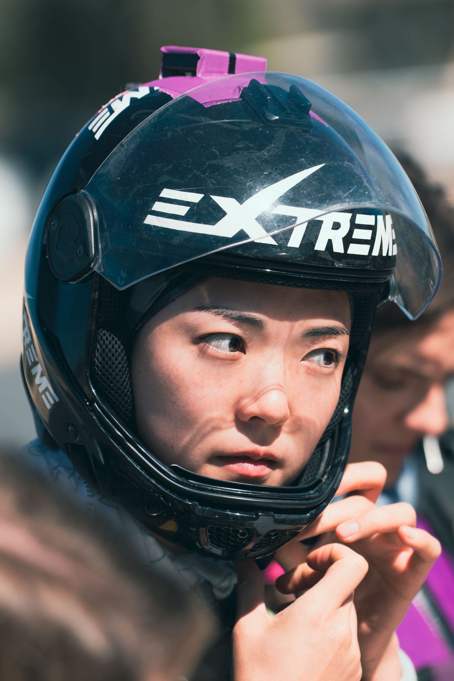 Person wearing a black and pink motorcycle helmet adjusting the strap.