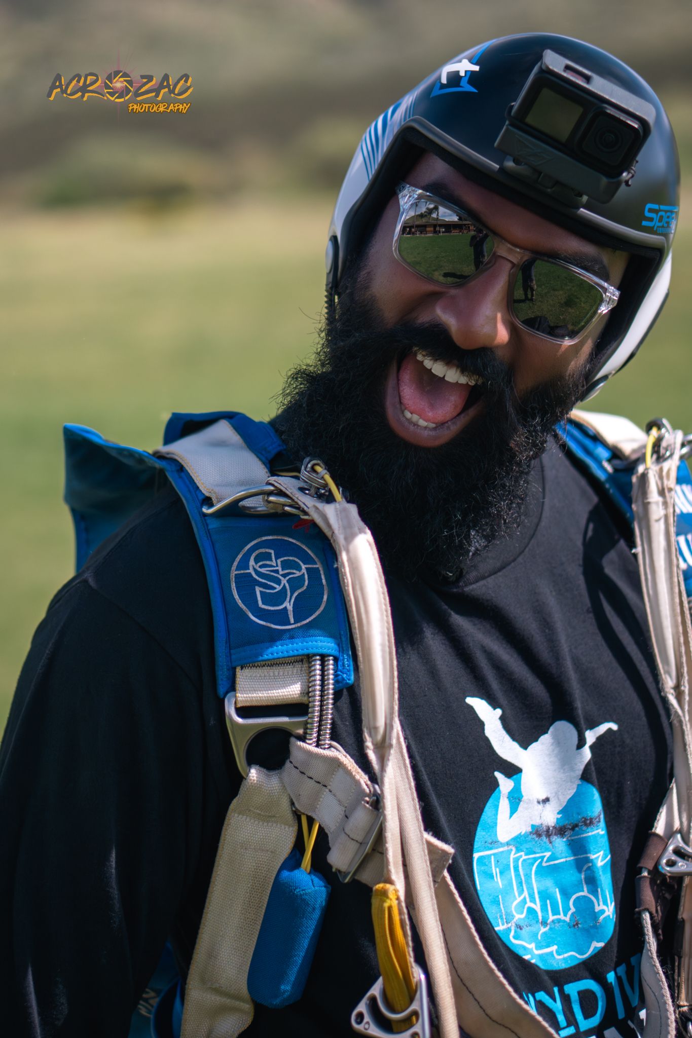 Person with beard laughing while wearing paragliding gear and helmet.