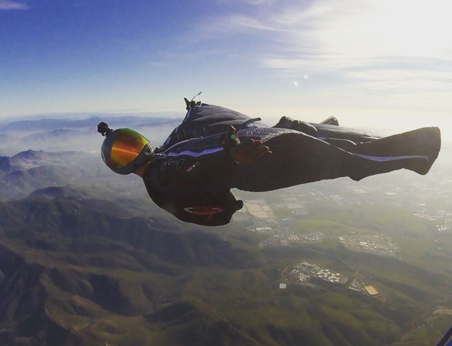 Skydiver gliding through sunset skies over mountainous terrain in a wingsuit.
