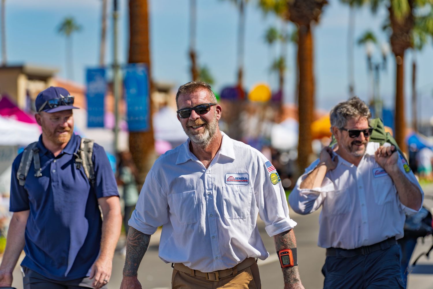Row of uniformed personnel walking along a sunny palm tree-lined street.