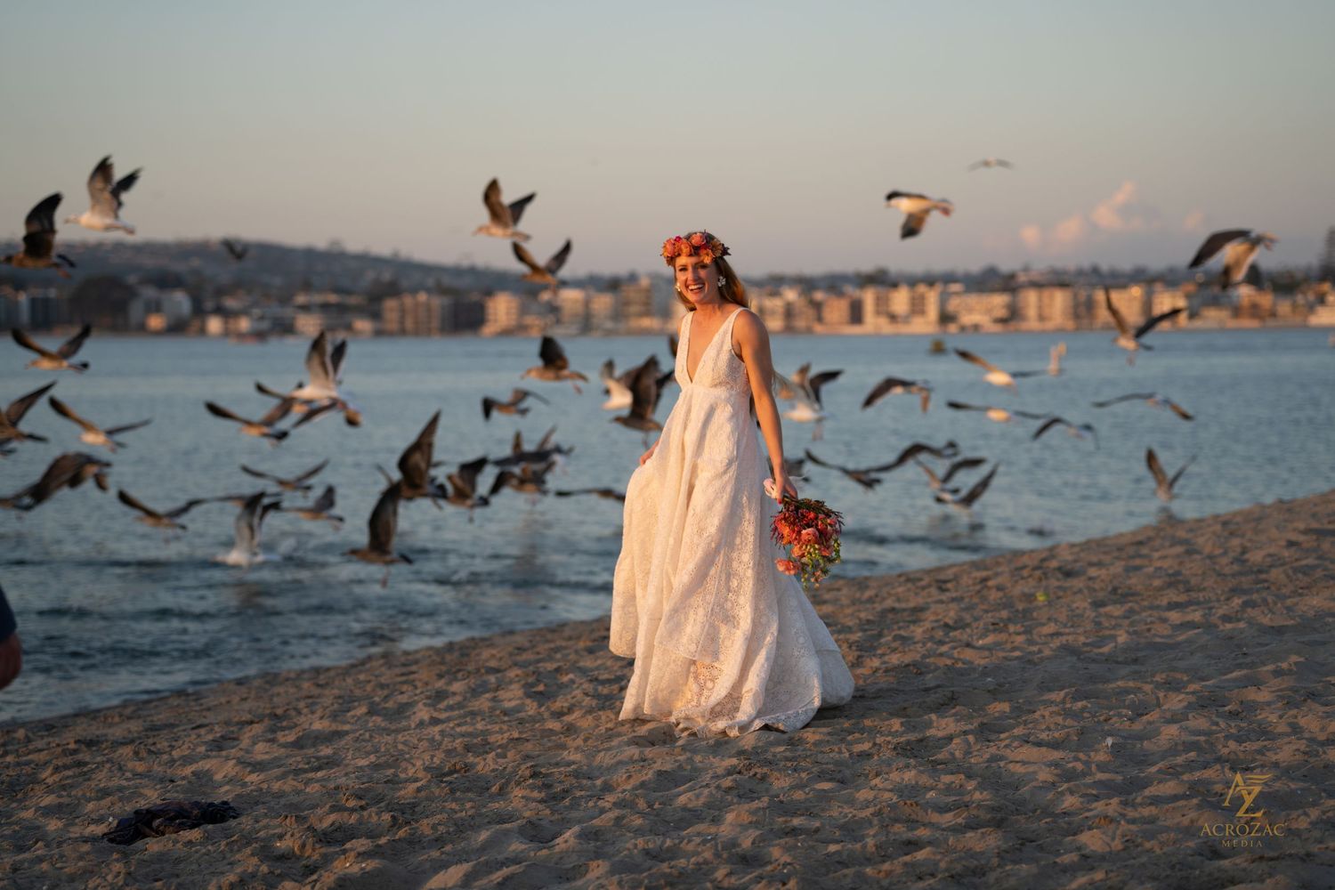 Seagulls take flight around couple during sunset beach photoshoot.