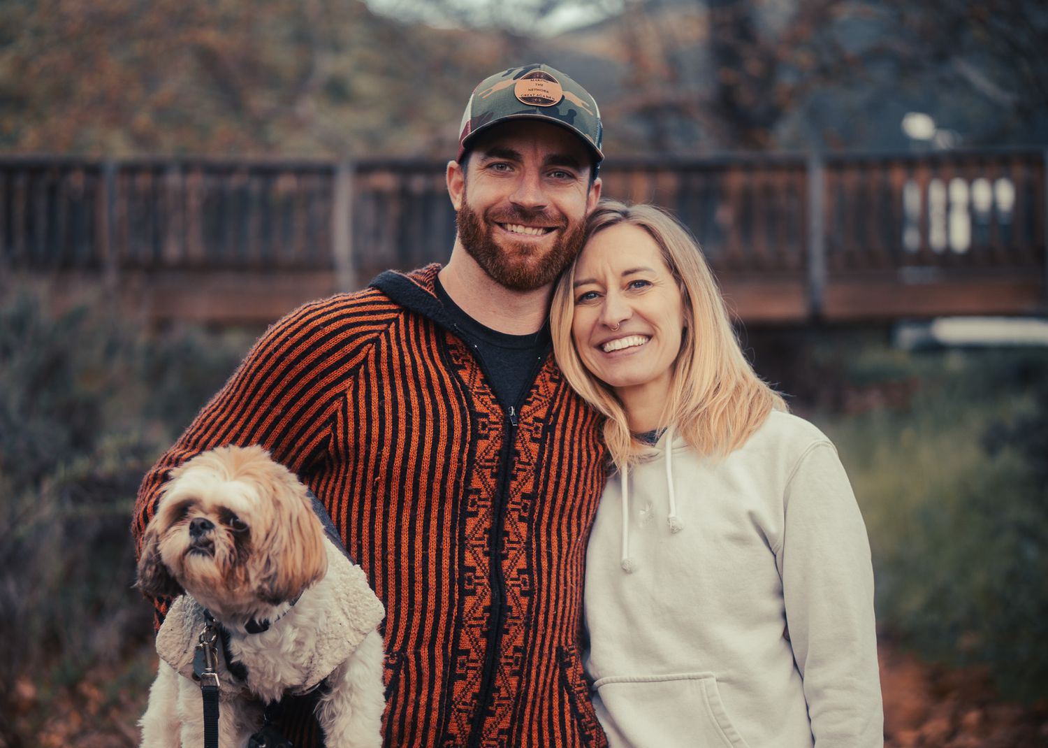 Outdoor autumn photoshoot featuring a couple and their small dog in casual attire.