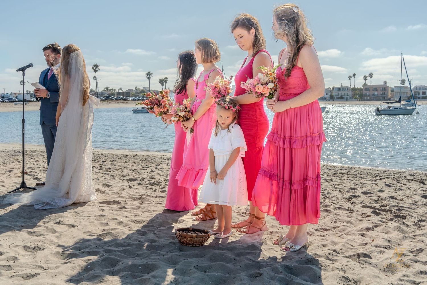 Wedding party in pink dresses poses together on a sunny beach.