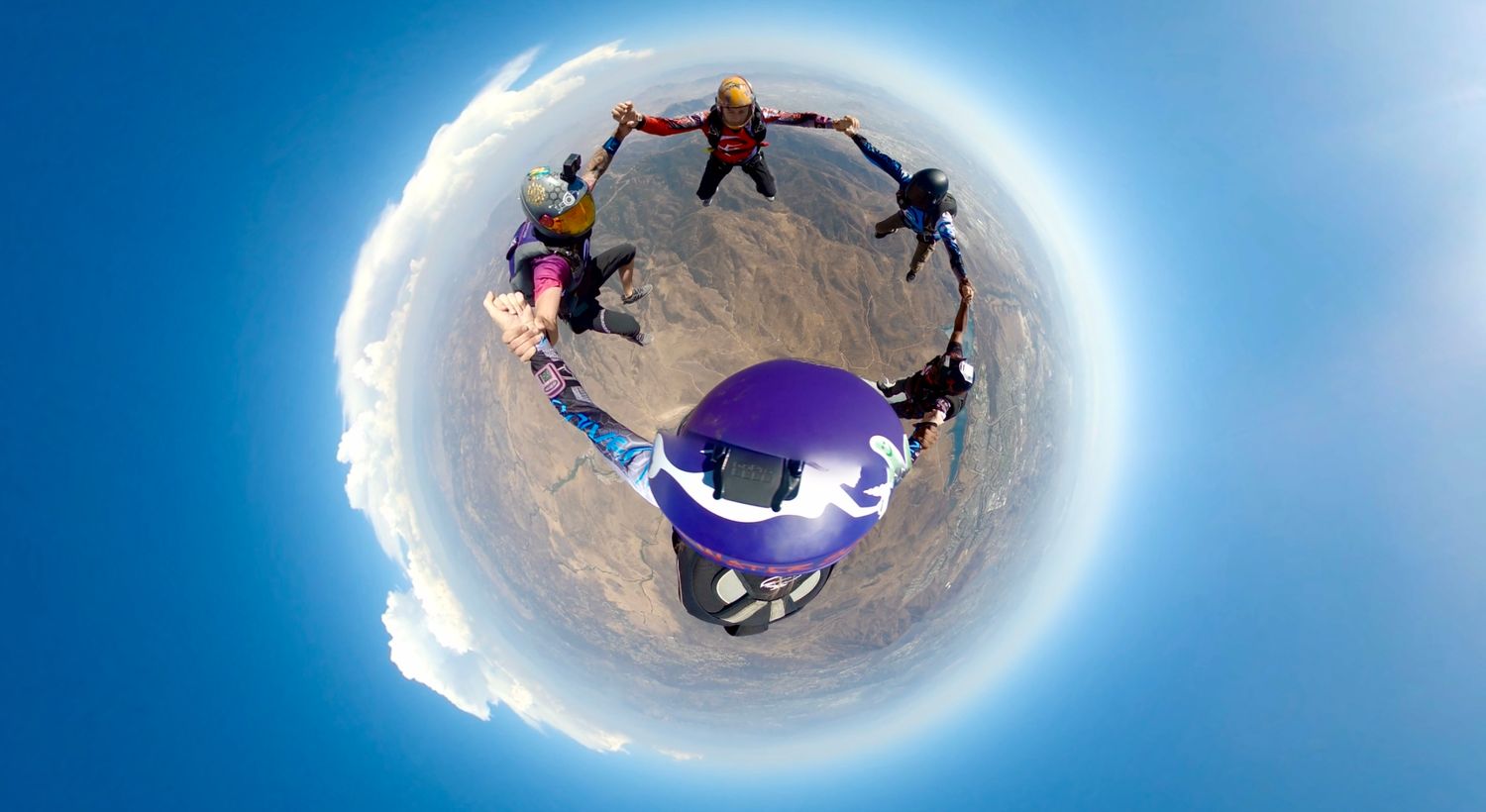 Aerial view of skydivers forming a circular formation against a bright blue sky.