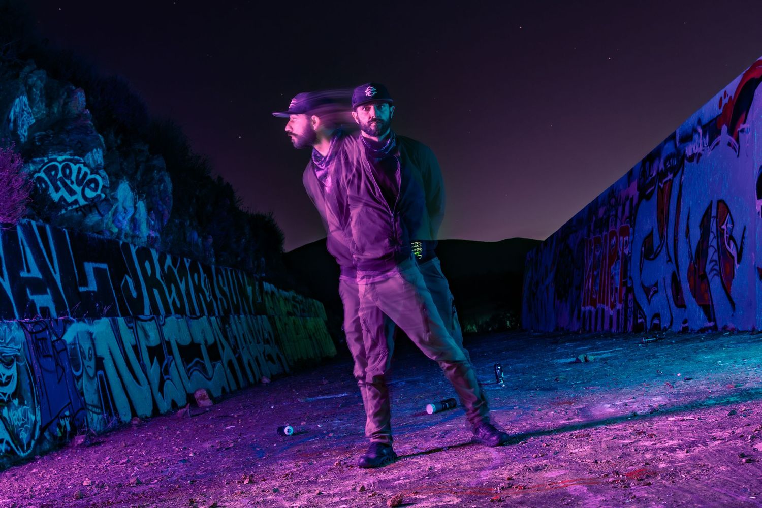 Night scene with colorful purple lighting illuminating rocky cliff formations.