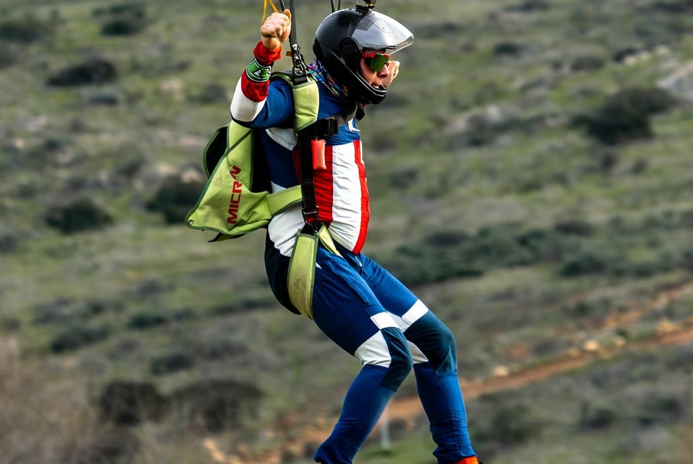 Skydiver in colorful jumpsuit performs aerial maneuvers during descent.