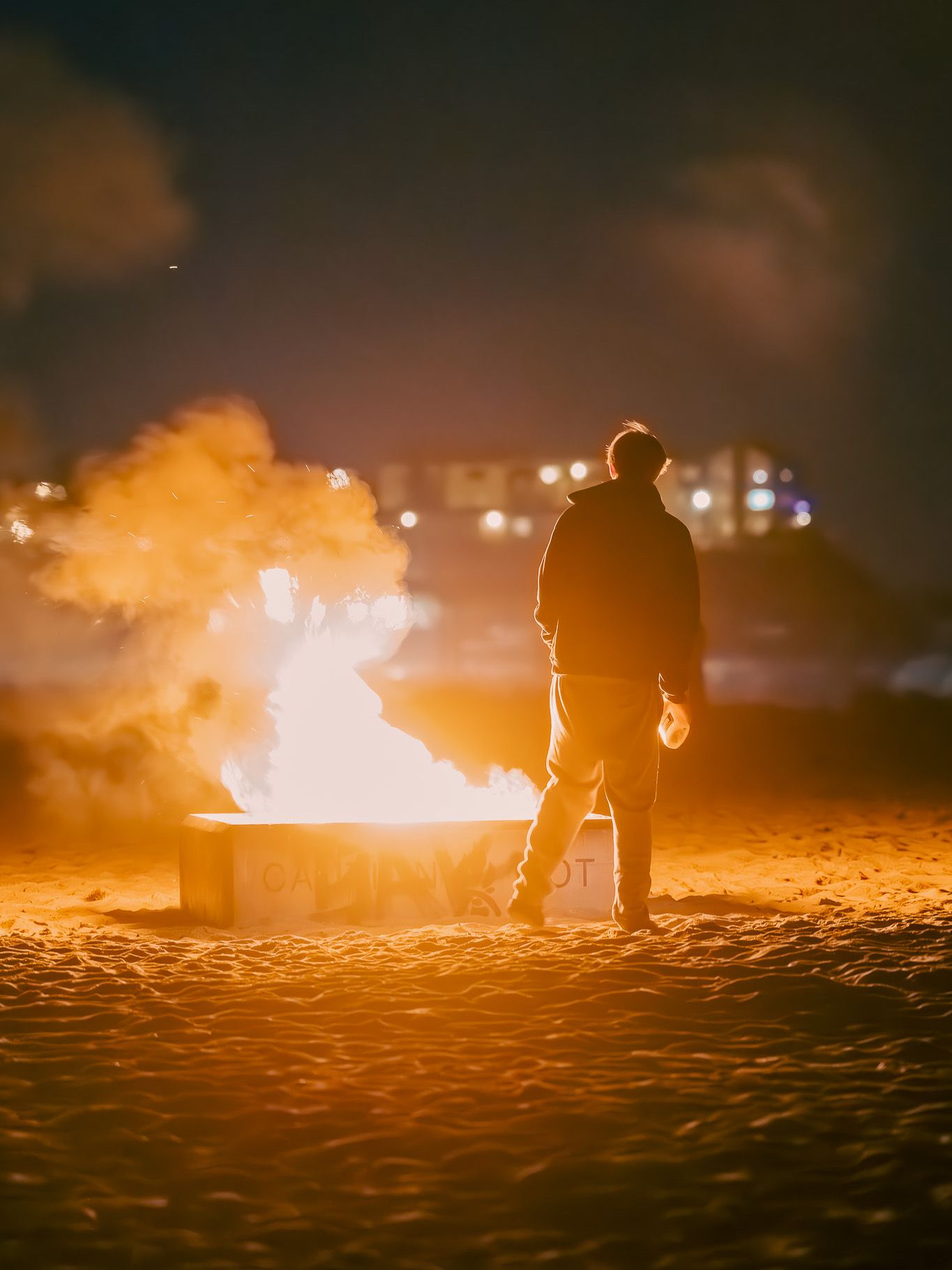 Silhouettes of people gathered around a bonfire on the beach at sunset.