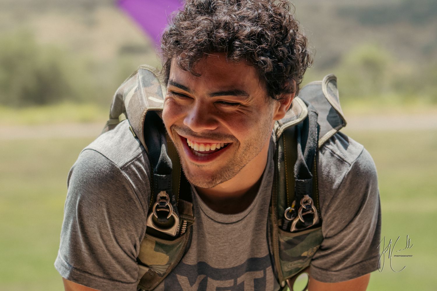 Person smiling while wearing outdoor gear in a sunny natural setting.