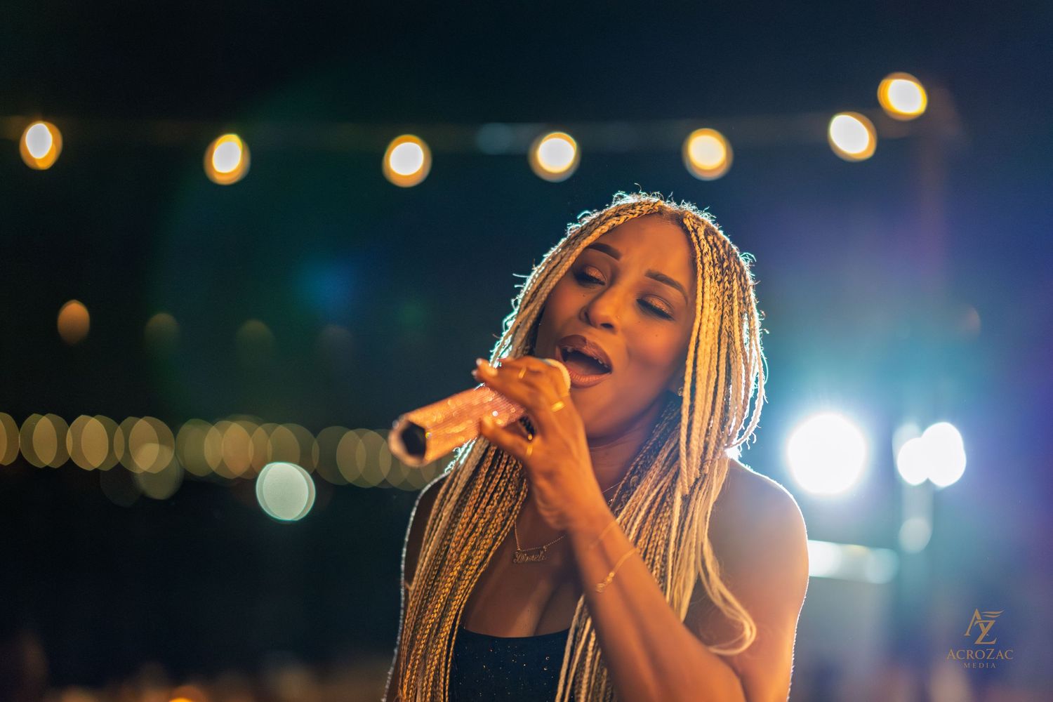 Concert performer singing on stage with dramatic blue lighting and string lights overhead.