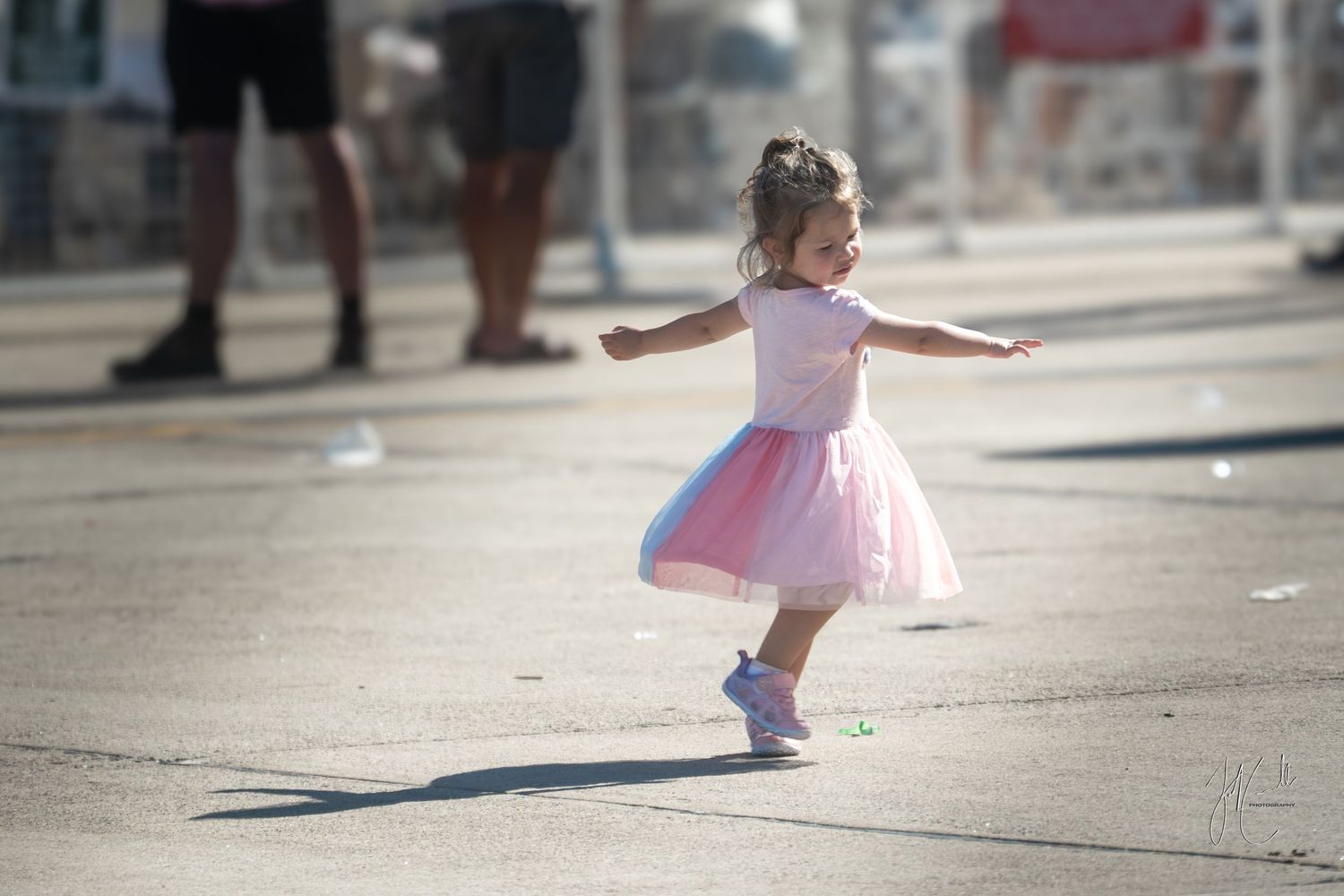 Small figure in pink tutu casting shadow while dancing on concrete.