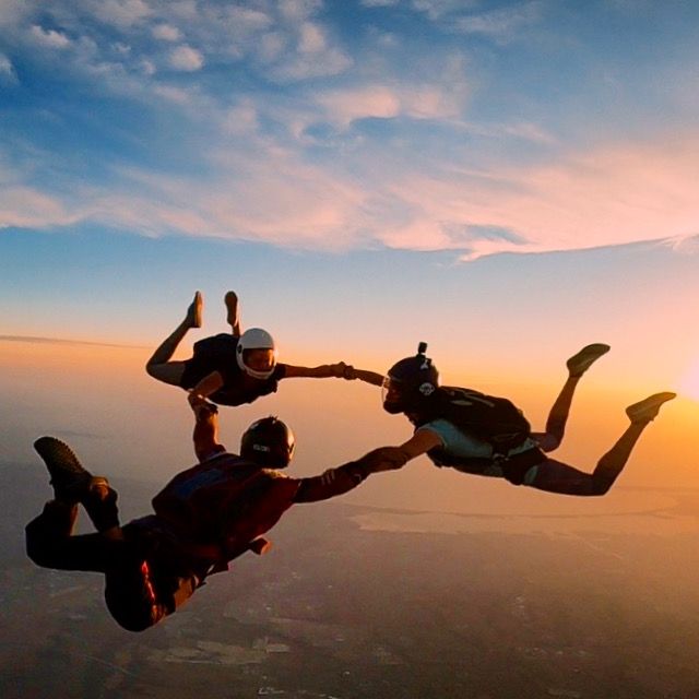 Skydivers performing formations during sunset with dramatic orange sky in background.
