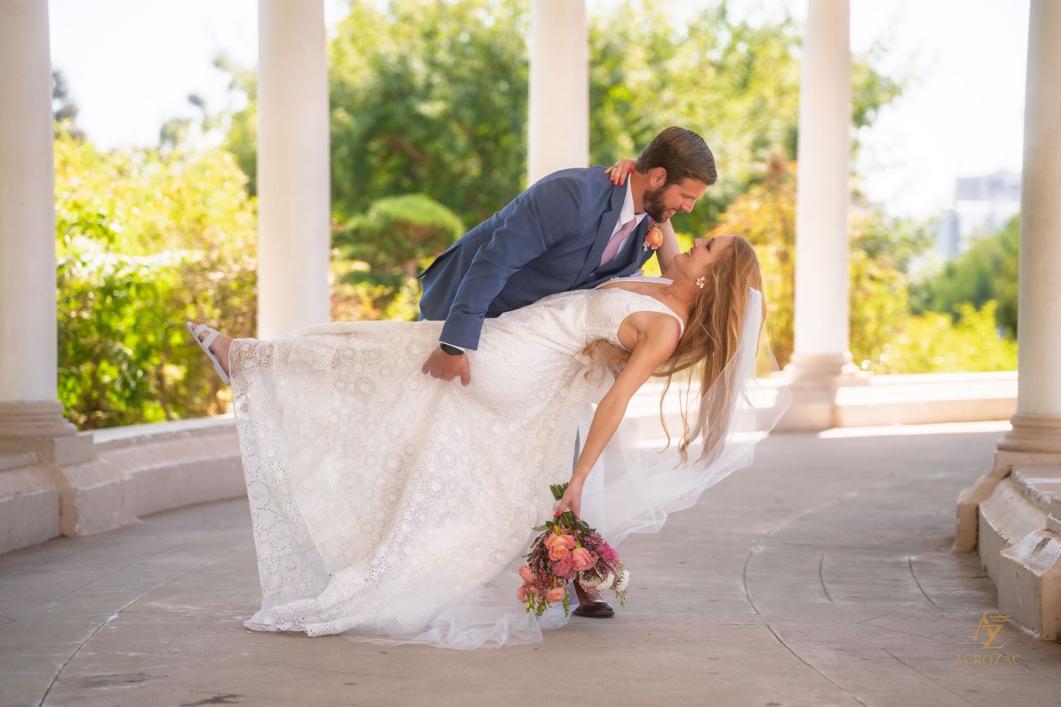 Wedding couple interacting playfully in an elegant columned outdoor setting.