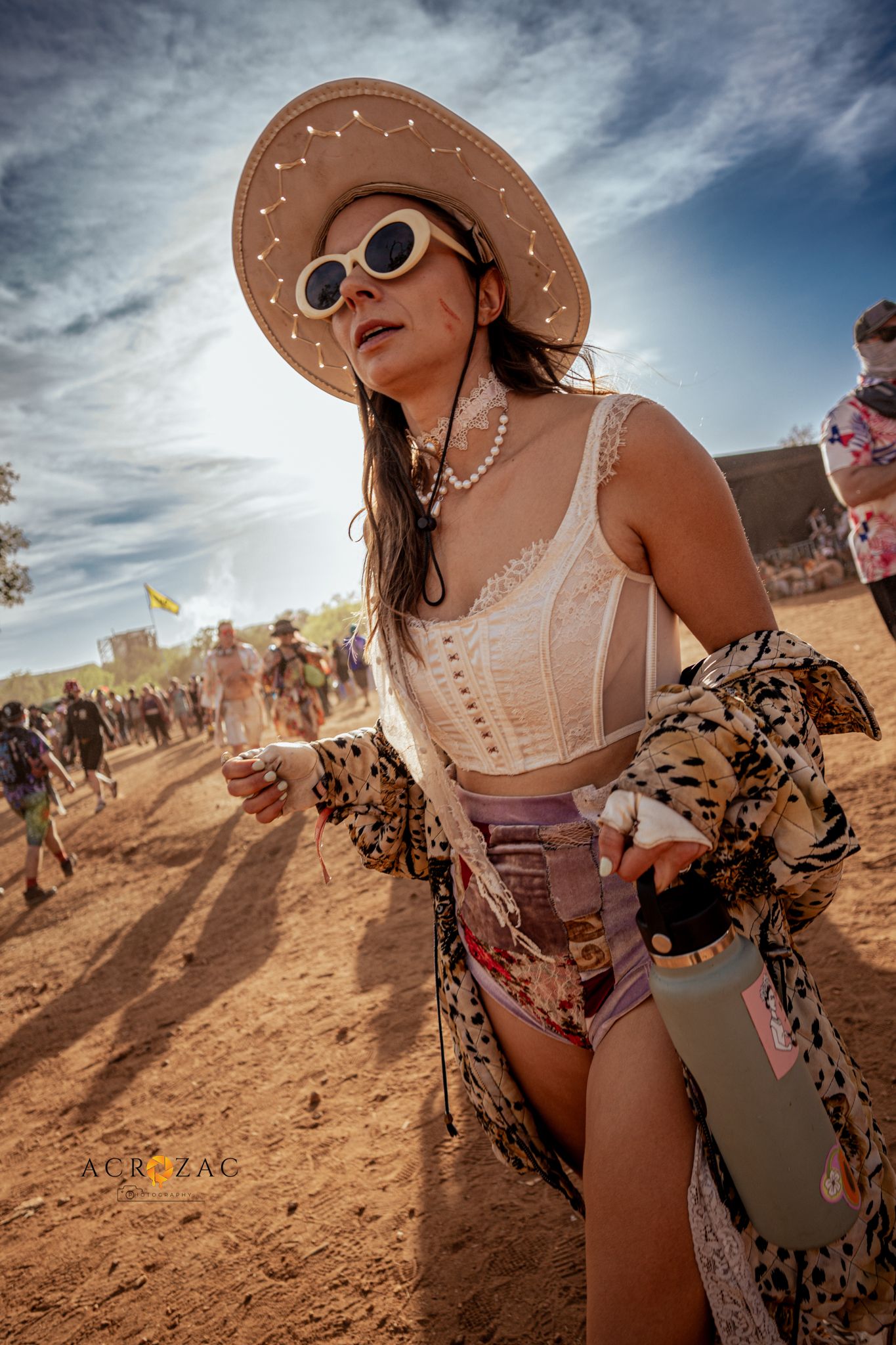 Festival-goer in western attire and sunhat enjoying a sunny desert gathering.