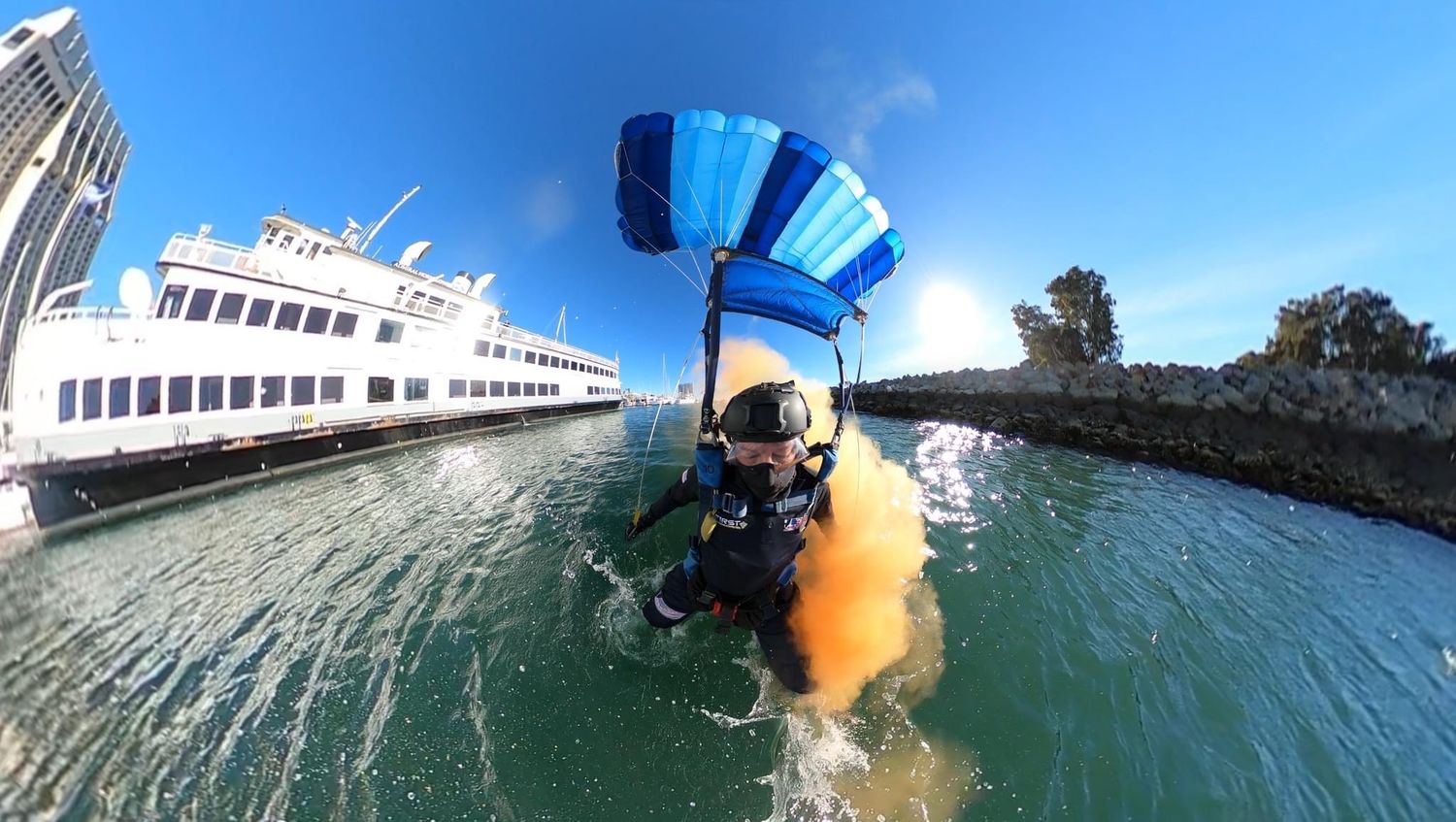 Skydiver with blue parachute landing near a large white cruise ship in the water.
