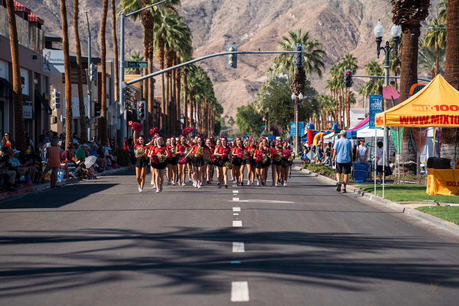 Street view of desert mountains behind palm trees with crowd gathered for event.